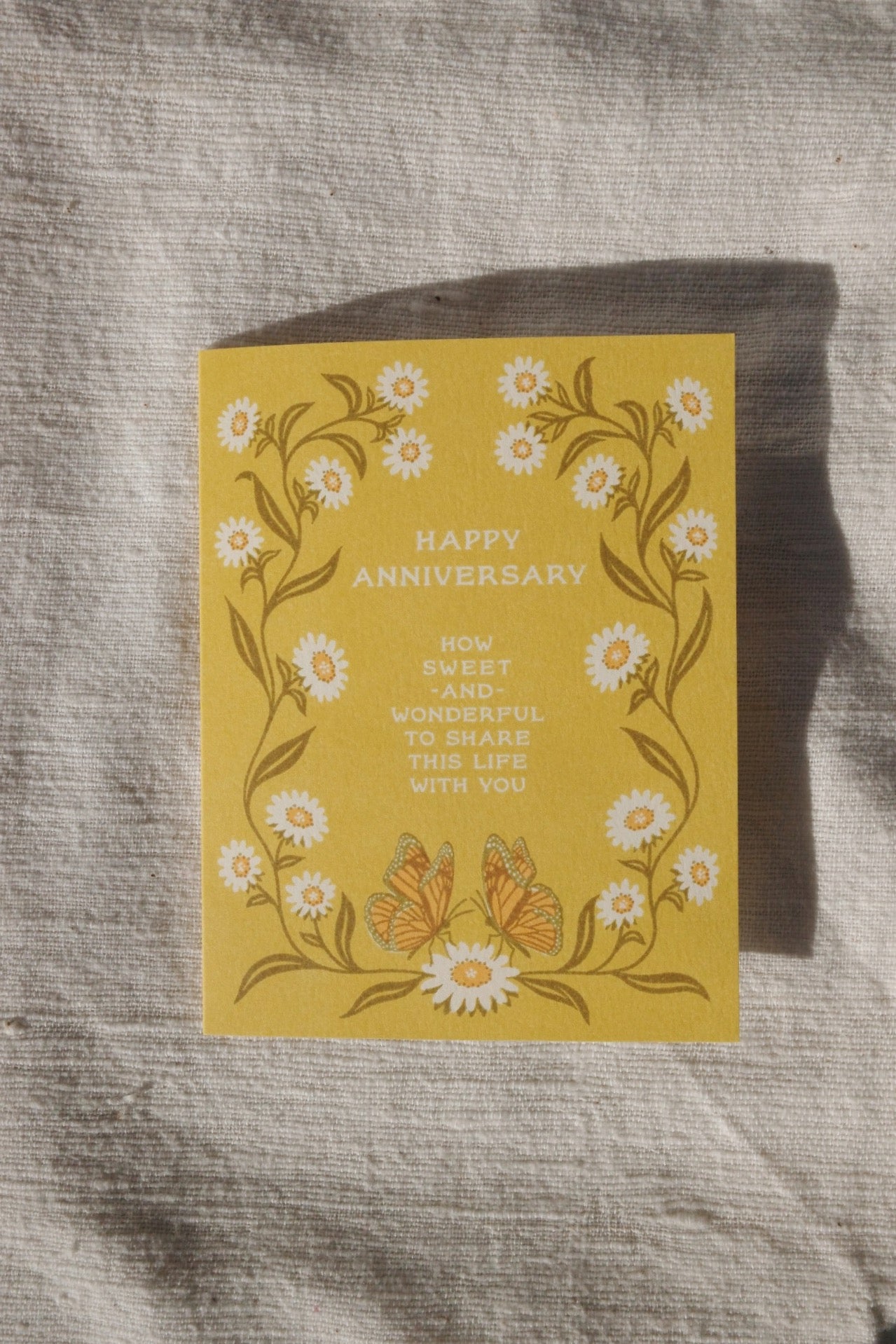 Yellow anniversary card with floral design and text on a textured surface